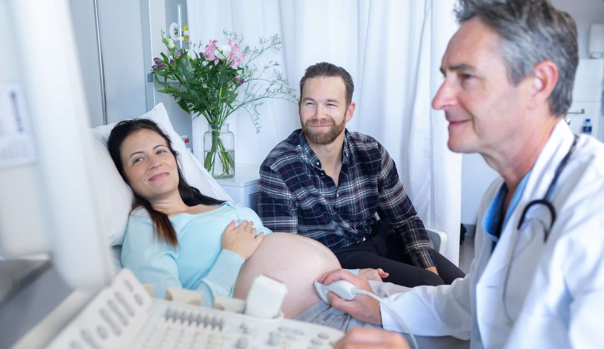 Side view of Caucasian male doctor doing ultrasound scan for pregnant woman in hospital Questions about delivering babies in the USA